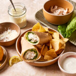 A bowl, filled with the chicken caesar wrap, sitting alongside a plate of chips on a countertop