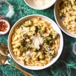 A bowl of the creamy one pot broccoli pasta, sitting on a table, alongside a bowl of Parmigiano Reggiano and a larger pot of pasta