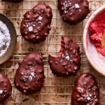 A wire cooling rack, topped with a few of the healthy strawberry peanut butter truffle eggs, with a bite taken out of one of the eggs