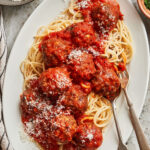 A plate of spaghetti, sitting on a countertop, topped with the ultimate meatballs and marinara sauce
