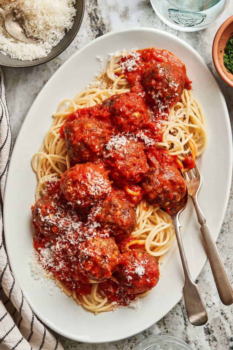 A plate of spaghetti, sitting on a countertop, topped with the ultimate meatballs and marinara sauce