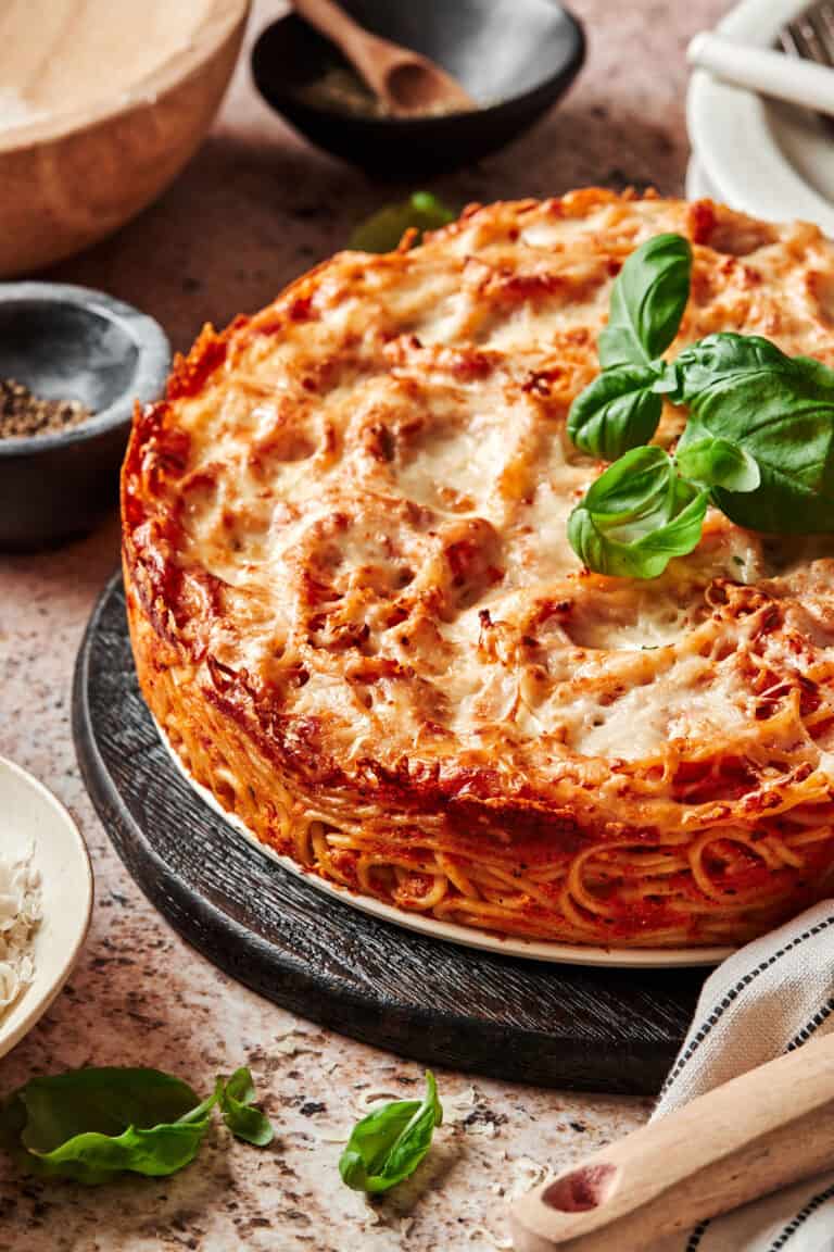 A close-up image of the whole spaghetti pie, topped with pieces of fresh basil and sitting on a countertop