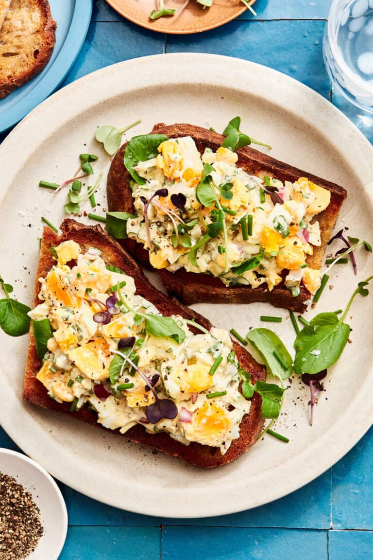 A plate of the one bowl healthy egg salad, spread across two pieces of toast, sitting on a countertop