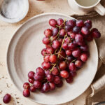 A bunch of perfectly cleaned grapes, sitting on a plate on a countertop