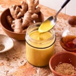 A jar of the Miso carrot dressing, sitting on a countertop alongside a bowl of ginger. A spoon is scooping the dressing out of the jar