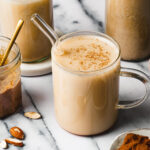 A glass of the homemade almond milk, sitting on a countertop with a straw in it