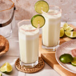 A tall glass of the Brazilian limonada, sitting on a countertop with a lime wedge on top of it