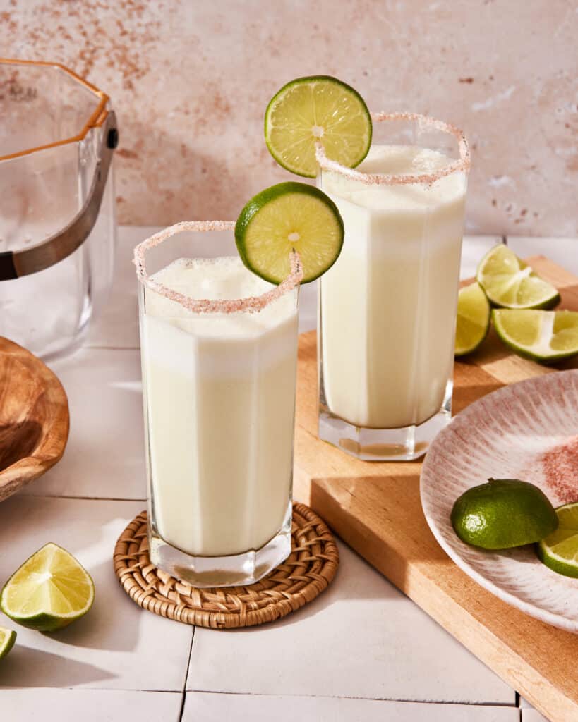 A tall glass of the Brazilian limonada, sitting on a countertop with a lime wedge on top of it
