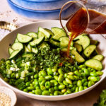 A bowl of the cucumber edamame salad, with the dressing actively being poured on top of it.