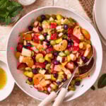 A large bowl of the ultimate fruit salad, sitting on a countertop, with serving spoons sitting inside of the bowl