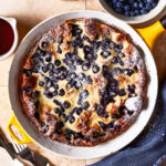 A pie dish, filled with the blueberry lemon dutch baby, sitting on a countertop