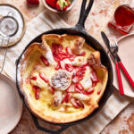 A cast iron skillet, filled with the strawberry lemon dutch baby, sitting on a countertop