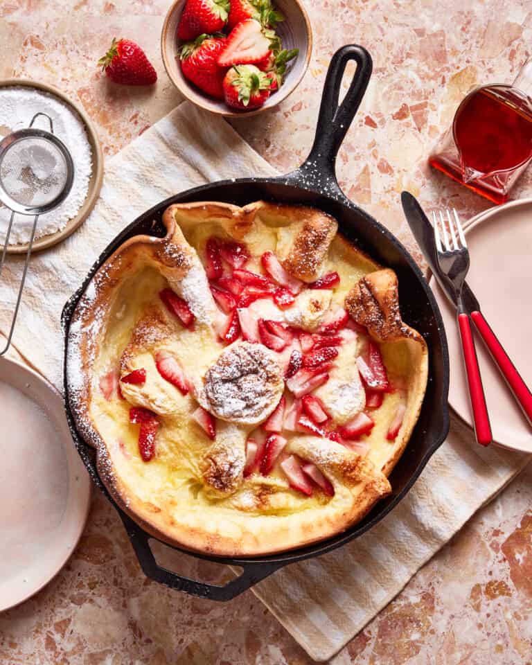 A cast iron skillet, filled with the strawberry lemon dutch baby, sitting on a countertop