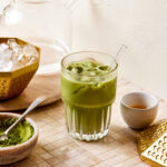 A glass of the best ever matcha latte, sitting on a countertop surrounded by a small bowl of matcha