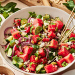 A bowl of the watermelon cucumber salad, sitting one a countertop with a pair of chopsticks sitting inside of the bowl