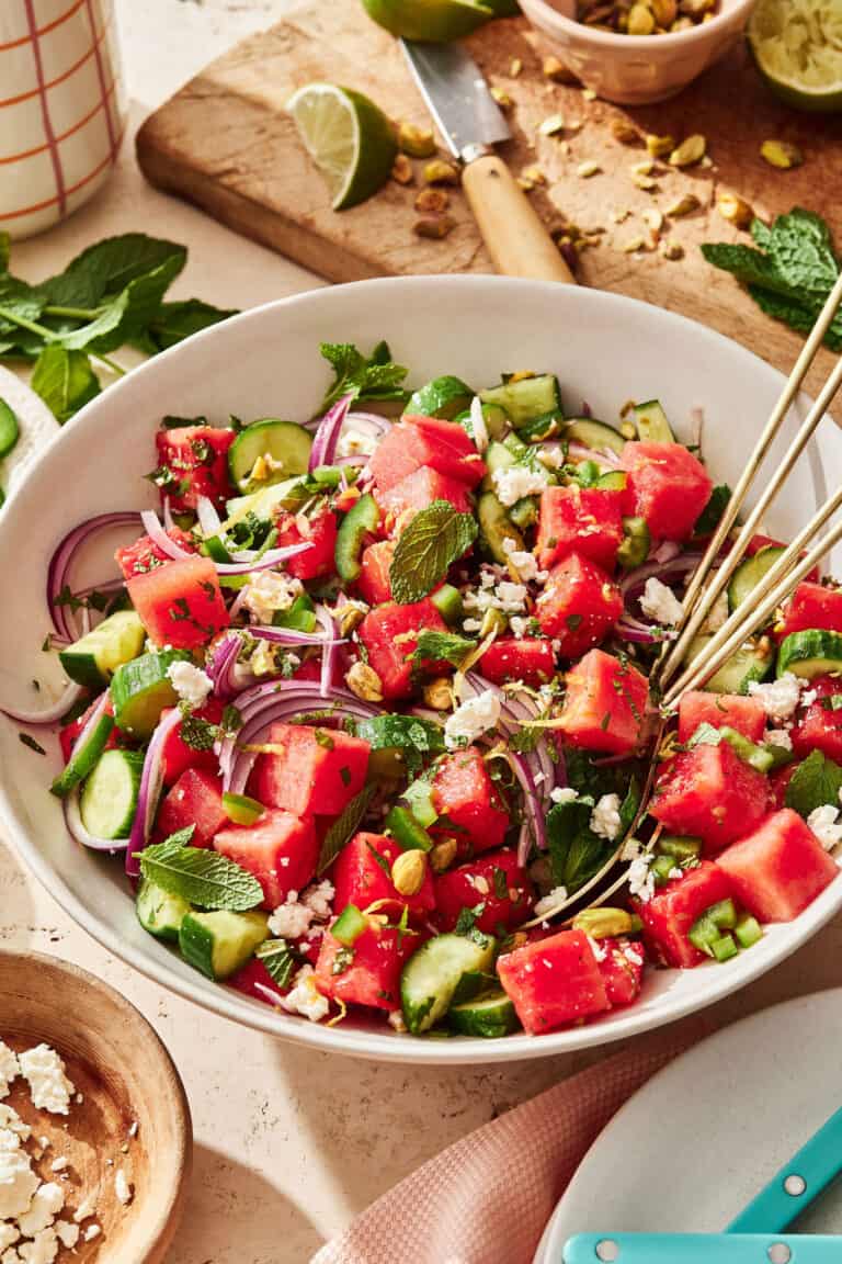 A bowl of the watermelon cucumber salad, sitting one a countertop with a pair of chopsticks sitting inside of the bowl