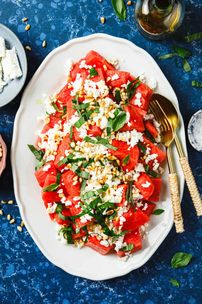 A plate of the watermelon feta salad, sitting on a countertop with serving utensils inside of it