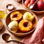 A bowl filled with the single serving olive oil baked peach and two scoops of vanilla ice cream