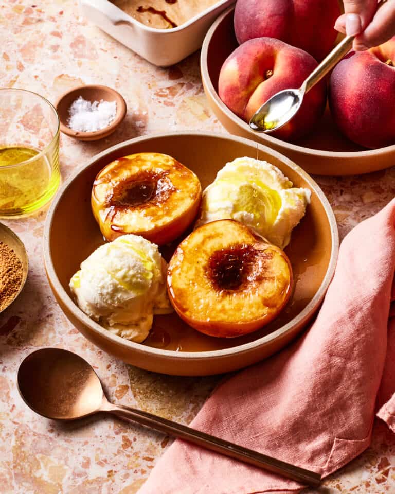 A bowl filled with the single serving olive oil baked peach and two scoops of vanilla ice cream