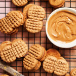 A bunch of the homemade nutter butters, sitting on a cooling rack next to a small bowl of peanut butter
