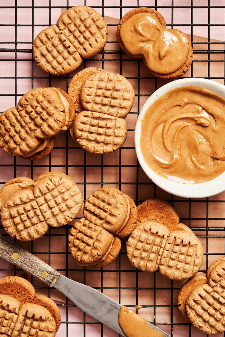 A bunch of the homemade nutter butters, sitting on a cooling rack next to a small bowl of peanut butter