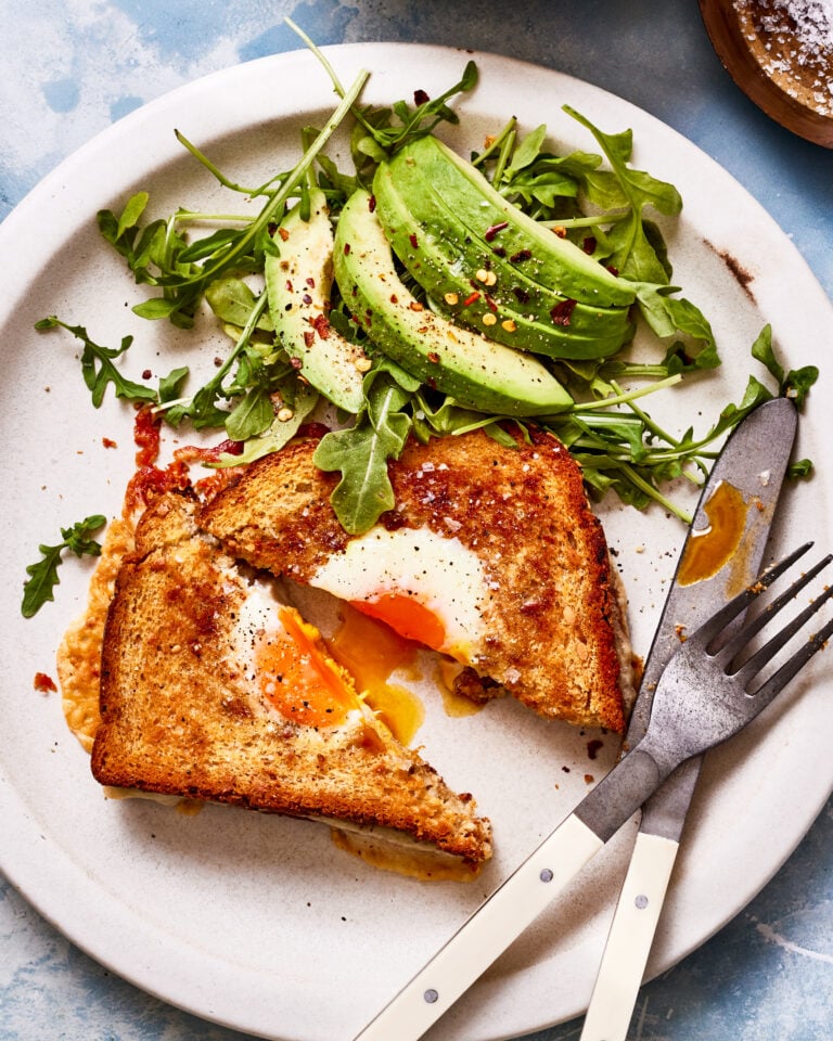 A plate, topped with the grilled cheese egg in a hole, next to an arugula and avocado salad
