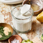 A jar full of the 5 minute healthy ranch dressing, sitting on a countertop with a spoon scooping some of the dressing out of the jar