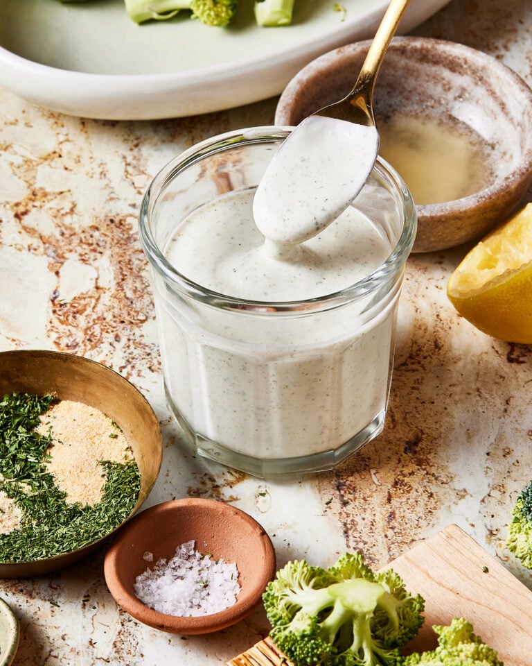 A jar full of the 5 minute healthy ranch dressing, sitting on a countertop with a spoon scooping some of the dressing out of the jar