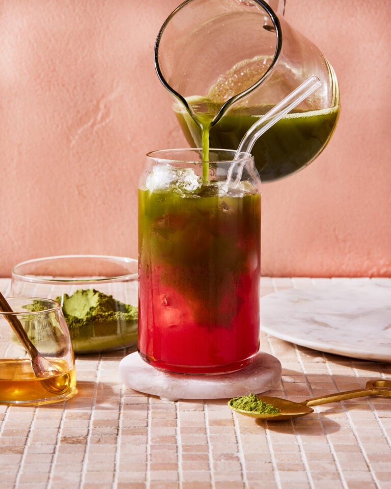 A glass of the watermelon matcha, sitting on a countertop with the matcha actively being poured into it