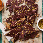 A tray of the pumpkin granola bark, sitting on a sheet of parchment paper with a knife next to it