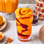 A glass of the copycat Erewhon Turmeric Crush Smoothie, sitting on a countertop surrounded by ingredients needed to make this smoothie
