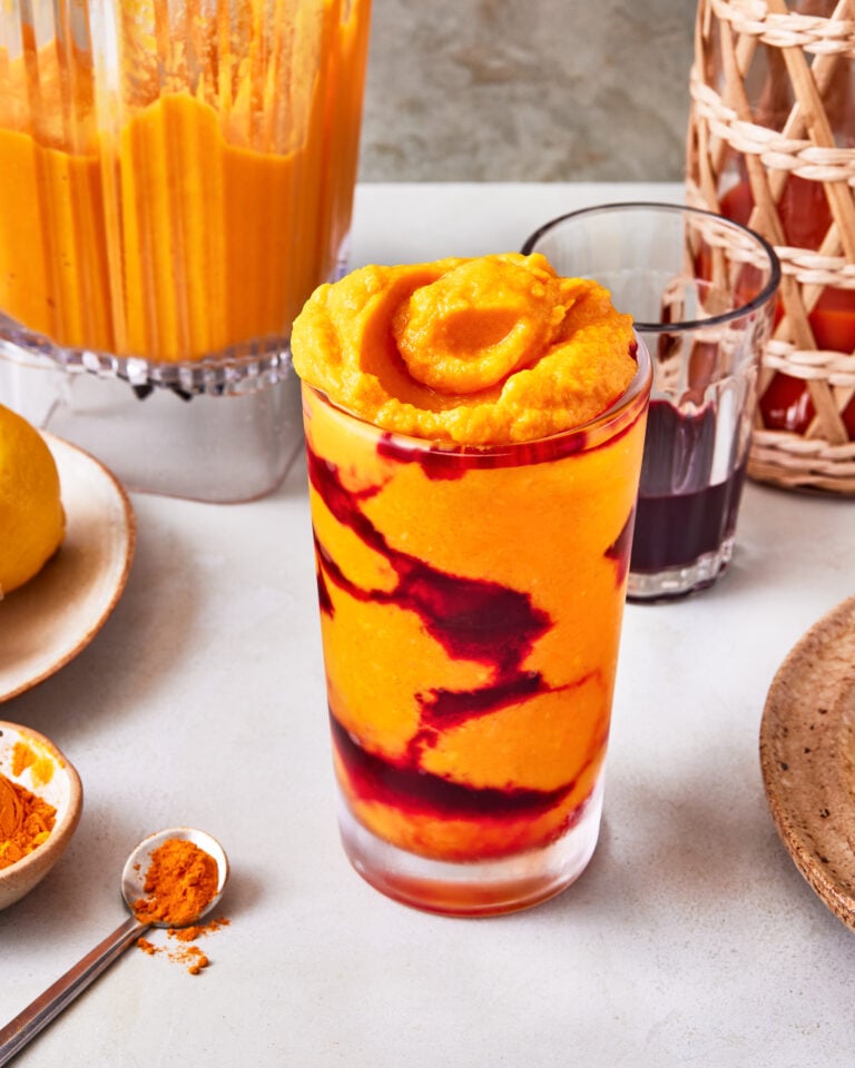 A glass of the copycat Erewhon Turmeric Crush Smoothie, sitting on a countertop surrounded by ingredients needed to make this smoothie