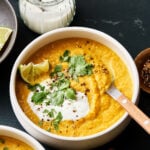 A close-up image of a bowl of the cauliflower lentil pumpkin soup, sitting on a countertop with a spoon resting in the bowl