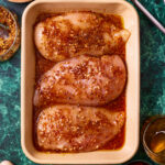 A ceramic tray filled with chicken breasts, topped with the honey mustard chicken marinade