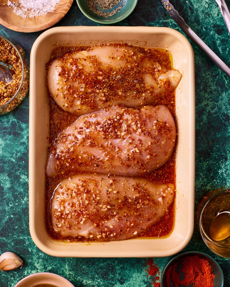 A ceramic tray filled with chicken breasts, topped with the honey mustard chicken marinade