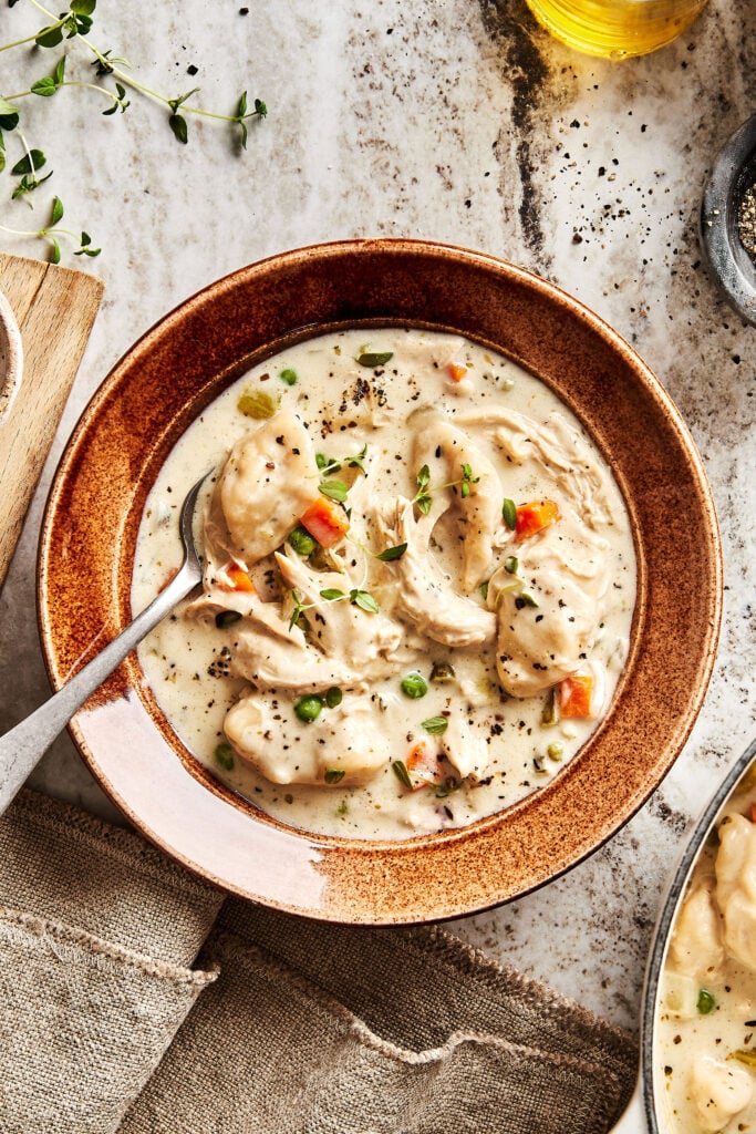 A bowl of the chicken dumpling soup, sitting on a countertop with a spoon resting on the edge of the bowl