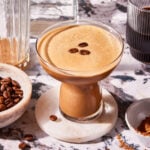 A glass of the pumpkin espresso martini, sitting on a countertop with some espresso beans