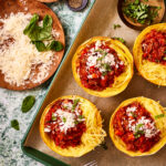 A baking sheet, lined with parchment paper, with the spaghetti squash boats sitting on top of it.