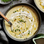 A bowl of the cozy potato leek soup, sitting on a countertop with a spoon sitting in the bowl