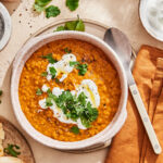 A bowl of the one pot curry lentil soup, sitting on a countertop next to a spoon and cloth napkin