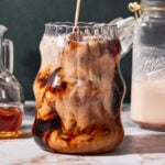A tall glass of espresso with the holiday nog creamer actively being poured into it