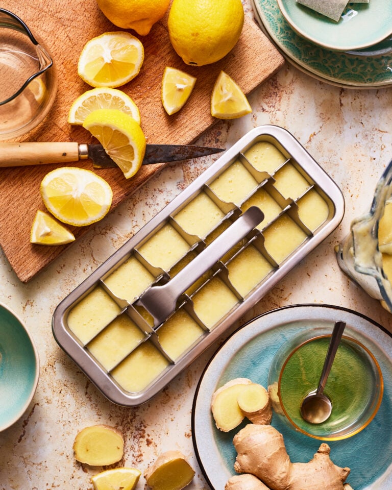 An ice cube tray, filled with the starbucks medicine ball immunity cubes, sitting on a countertop next to lemons