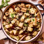 A pot of the sourdough wild mushroom stuffing, sitting on a countertop with a spoon resting inside of the bowl