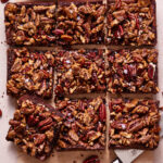 A sheet of the pecan fudge brownies, sitting on a sheet of parchment paper on a countertop, sliced into squares