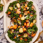A plate of the warm roasted veggie salad, sitting on a countertop with serving utensils next to it
