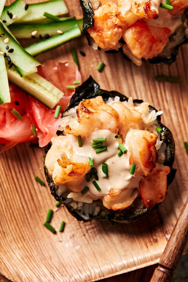 A close-up image of one of the viral shrimp sushi cups, sitting on a plate next to chopped vegetables