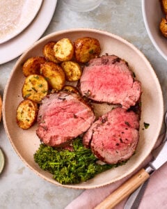 The sliced beef tenderloin, sitting on a plate next to crispy smashed potatoes and grilled broccolini