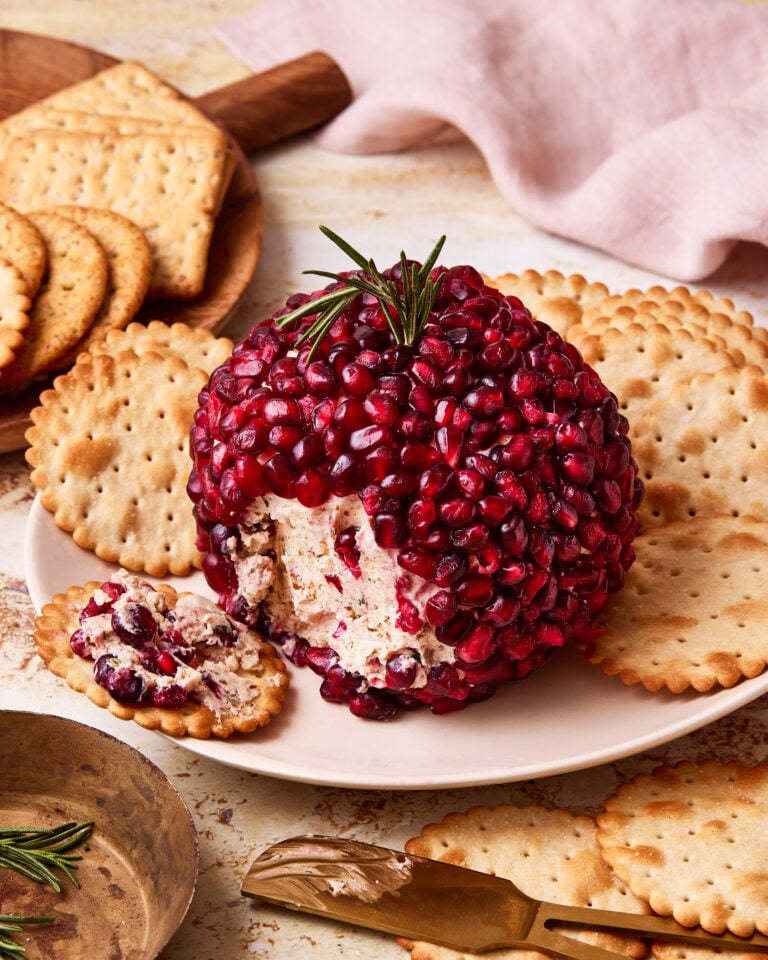 A close-up image of the holiday cheese ball, sitting on a plate next to crackers