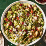 A plate of the shaved brussels sprouts salad, sitting on a countertop with serving utensils sitting inside of the bowl
