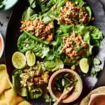 A plate of the peanut chicken lettuce wraps, sitting on a countertop with a small bowl of sauce sitting next to them